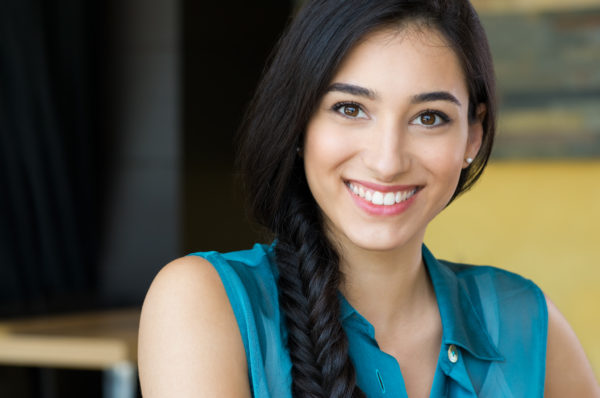 Closeup shot of young woman smiling. Portrait of brunette girl looking at camera and smiling. Shallow depth of field with focus on beautiful young happy girl with braid smiling.