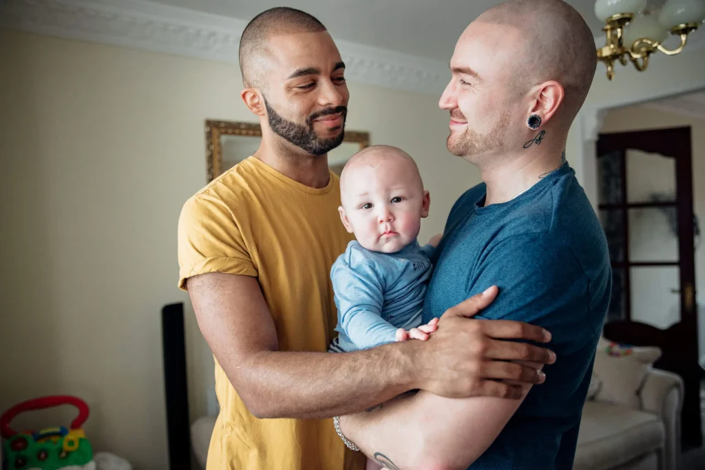 Gay Couple spending time with their little baby boy. They're all together at home standing in an embrace